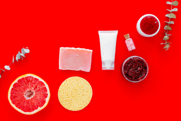 Scrabs, soap and creams for natural cosmetic set with herbs and grapefruit on red background top view