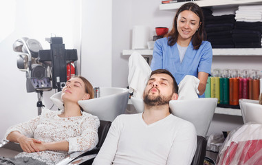 Obraz premium Female professional washing cheerful male's hair in salon