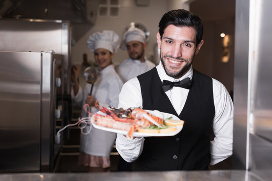 Waiter holding seafood dish in kitchen of restaurant
