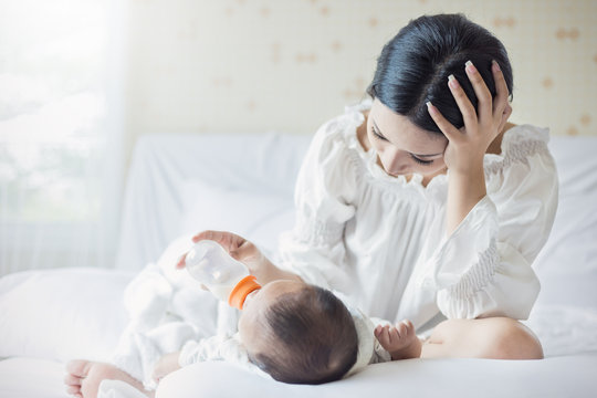 portrait of Asian mother nursery feeding bottle of formula milk to newborn baby in bed suffering from post natal depression. Health care single mom motherhood stressful concept.