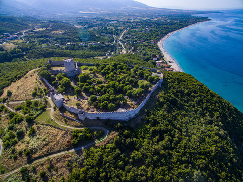 An aerial perspective of the medieval castle of platamonas on the top of a green hill looking down at the beach. 