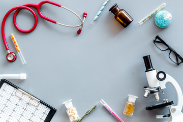 Do medical research with microscope, stethoscope, pad, pills and test tube on gray background top...