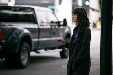 Female pedestrian waiting for a rideshare.  She is sharing her gps location via cellphone app so...