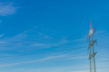 Low angle view of high voltage post and electric cable against sunny blue sky. Uprisen angle of electricity post.