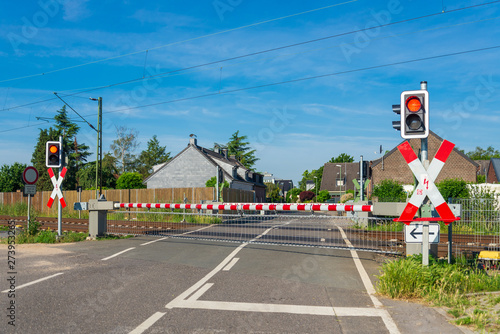 Leinwandbilder Outdoor Sunny Street View Of Level Crossing Railway Barrier And Red Traffic Light At Intersection Between Road And Railway In Small Village Meerbusch Countryside Of Dusseldorf Germany Peeradon