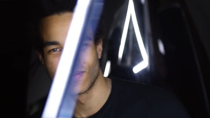Close up of young handsome mixed-race man looking at camera and smiling against black background with triangular neon lamps - Powered by Adobe