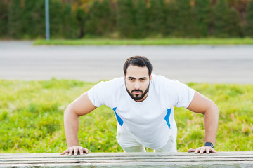 Portrait sporty man 30s in sportswear doing push-ups in green park