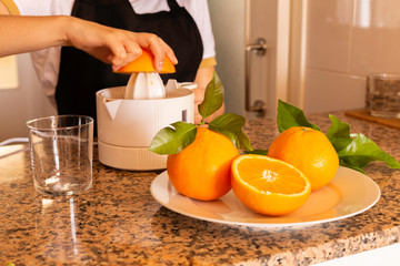 Detail of a teen's hands holding a citrus juicer with orange half and freshly squeezed citrus