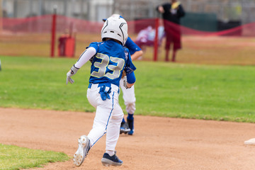 Youth baseball player in blue uniform and white helmet sprints across infield to steal second base.