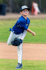 Youth baseball player in blue uniform following through on throw made in the infield during a game.