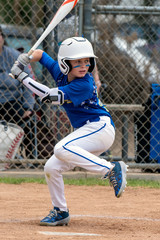 Youth baseball player in blue uniform and white helmet lifts leg in preparation to hit and swing...