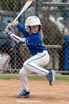 Youth baseball player in blue uniform and white helmet lifts leg in preparation to hit and swing the bat.