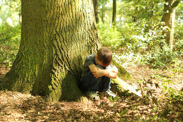 boy, schoolboy sits sad, under a tree, his head on his hands in the forest