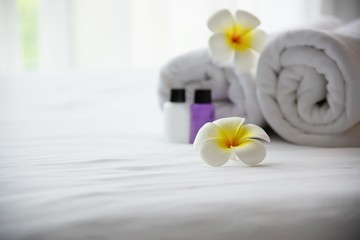 Fototapeta na wymiar Hotel towel and shampoo and soap bath bottle set on white bed with plumeria flower decorated - relax vacation at the hotel resort concept