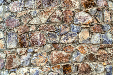 Multi-colored background of untreated natural stone, on the facade of the old oval tower of stones of different breeds and shades