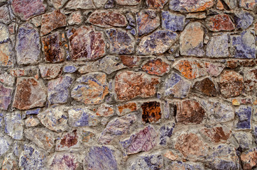 Motley background of stones of different breeds and shades of raw natural stone on the facade of the old oval tower