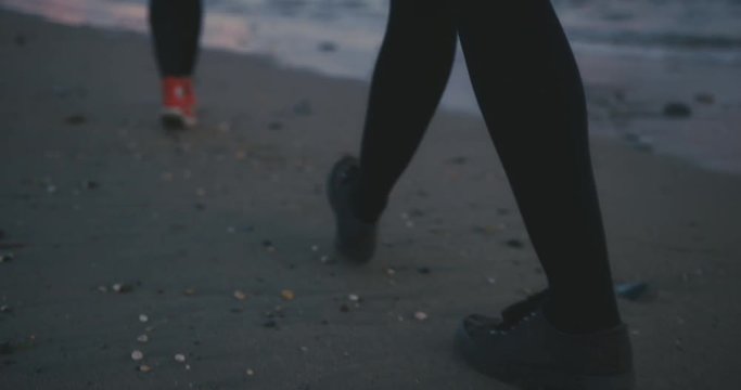 The feet and legs of two young women walking on the beach after sunset
