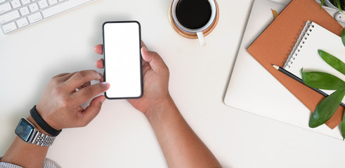 Cropped shot top view of businessman hands using smartphone mockup at the white office desk