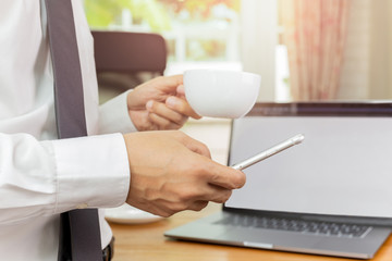 Businessmans hand holding cellphone and cup of coffee in his office.