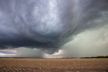 A supercell thunderstorm dumps heavy rain and hail over an empty field.