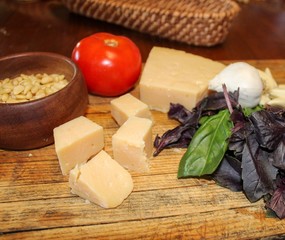 Ingredients for making home made pesto including parmesan cheese, fresh purple and green basil, garlic and pine nuts on wooden board