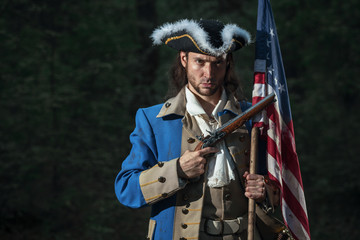Man dressed as soldier of War of Independence United States aims from pistol with flag.  4 july...