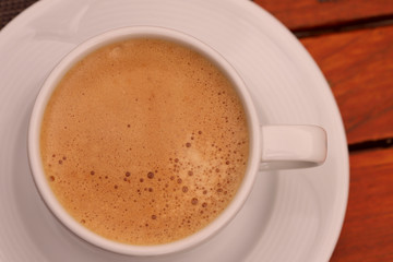 White cup of coffee with coffee foam on the table. Horizontal, cropped shot, top view, close-up. Coffee concept