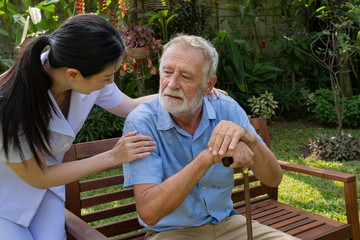 senior man sitting with memory lost and smiling nurse, takes care and discussion and cheer in the garden at nursing home