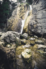 Beautiful waterfall with trees, red leaves, rocks and stones in autumn forest.