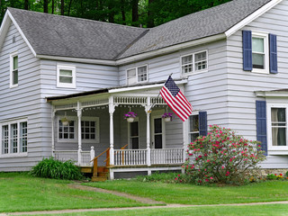 traditional style clapboard house with large porch and American flag
