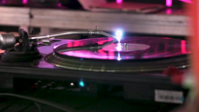 Close shot of a the turntable of a dj moving in slow motion in a party with pink lights.