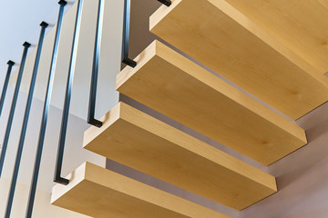 Floating stairs. Ash lumber stairs with railing attached to brown wall and leading to second floor...