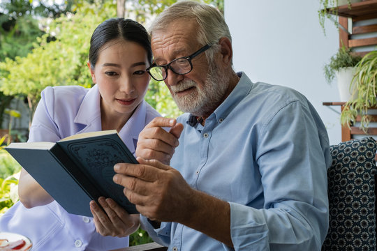 senior man happiness with smiling nurse, read book together at balcony near garden at nursing home