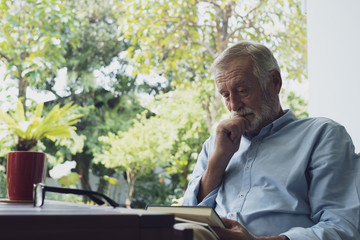 senior man happiness sitting and reading book at balcony near garden at nursing home for relaxing