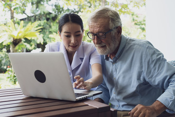 senior man and nurse, teaching and using laptop at balcony near garden at nursing home for internet online together