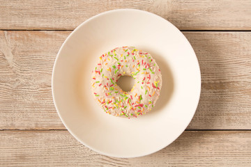 Fresh glazed donut with colorful sprinkles on a white plate.