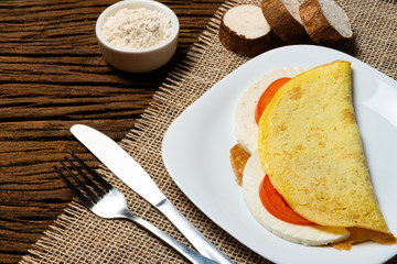 Crepioca. Pancake of cassava (tapioca) with cheese and tomato on plate on old wooden background. Selective focus.