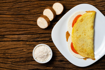 Crepioca. Pancake of cassava (tapioca) with cheese and tomato on plate on old wooden background. Selective focus.