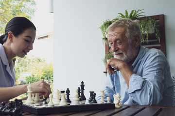 senior man happiness and nurse, playing chess at balcony near garden at nursing home together