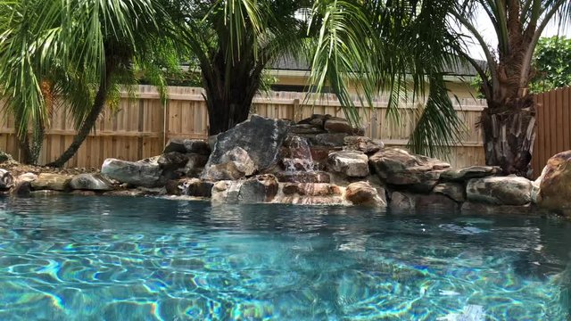 Peaceful outdoor pool setting with palm trees, blue salt water and a bubbling waterfall.