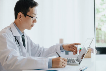 Fototapeta na wymiar Doctor in hospital writing medical documentation and using laptop