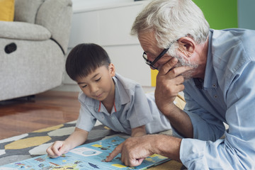 senior man happiness and grandson are sitting on the floor and playing games and reading book at living room together