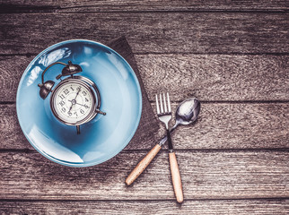 One vintage clock in blue ceramic dish with fork and spoon on wood table top view.
