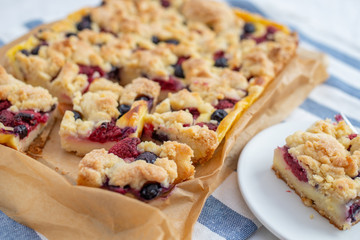 Sweet delicious crumble cake in a baking form and pieces of the cake on a table