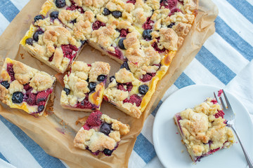 Sweet delicious crumble cake in a baking form and pieces of the cake on a table