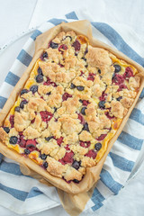 Sweet delicious crumble cake in a baking form and pieces of the cake on a table