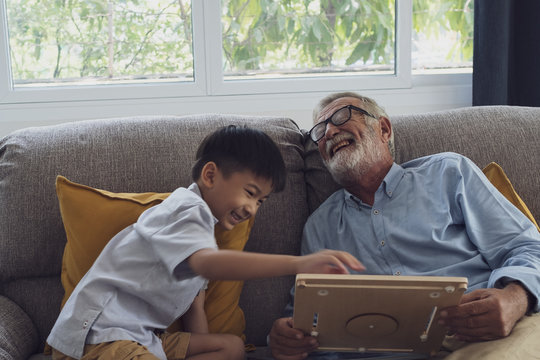 senior man happiness and grandson are sitting on the sofa and playing games and reading book at living room together