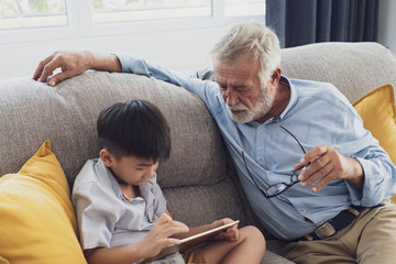 senior man happiness and grandson are sitting on the sofa and playing games and using tablet at living room together