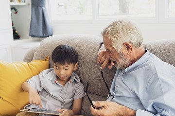 Obraz premium senior man happiness and grandson are sitting on the sofa and playing games and using tablet at living room together
