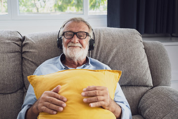 senior man happiness sitting on the sofa and listening music with headphone at living room for...